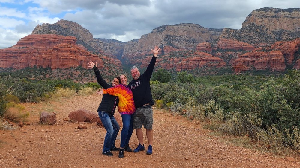 Vibrant red rock formations, expansive desert landscapes, dramatic sky at sunset, lush greenery in the foreground, striking geological patterns, ethereal light casting shadows, serene atmosphere, panoramic view of Sedona's natural beauty.